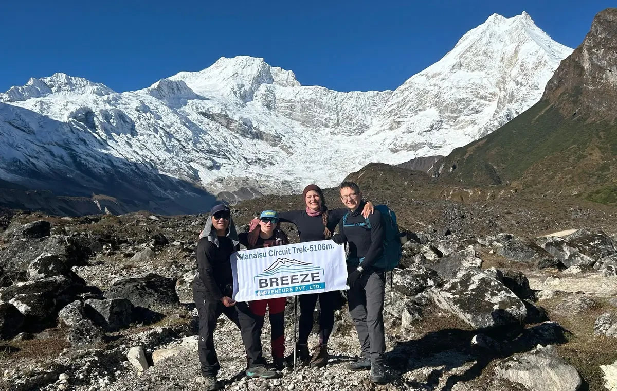 Trekkers holding a Breeze Adventure banner at Manaslu Circuit Trek high point, 5106m, with snow-capped Manaslu peaks behind