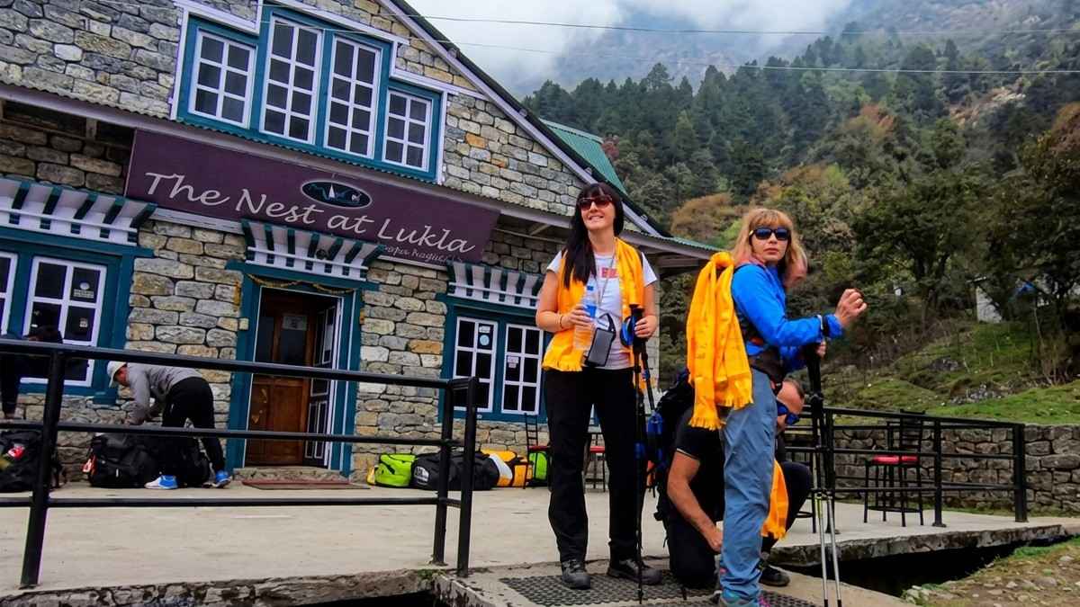 Two trekkers with orange khata scarves and poles standing outside The Nest lodge in Lukla before the Everest Base Camp trek