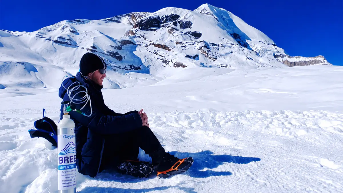 Trekker resting with portable oxygen cylinder to manage altitude sickness symptoms at high altitude in the Himalayas