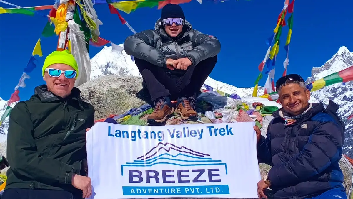Trekkers holding Breeze Adventure Langtang Valley Trek banner at summit with prayer flags Nepal