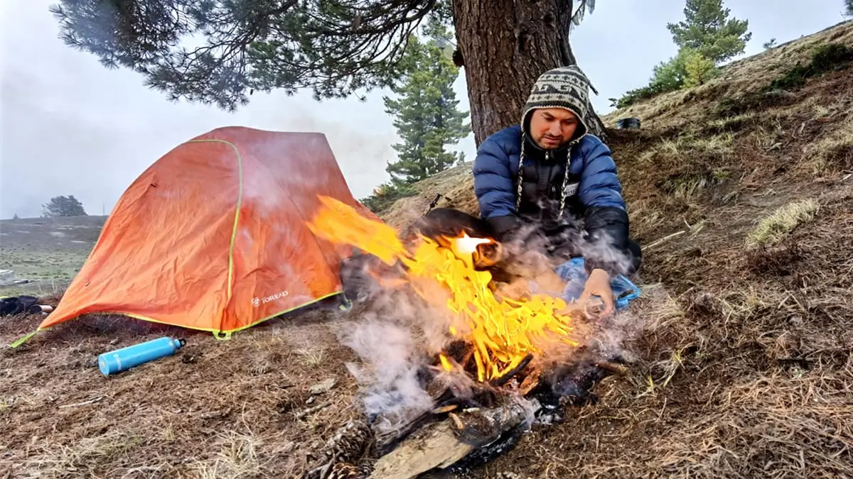 Trekker lighting campfire beside orange tent during Nepal trekking adventure