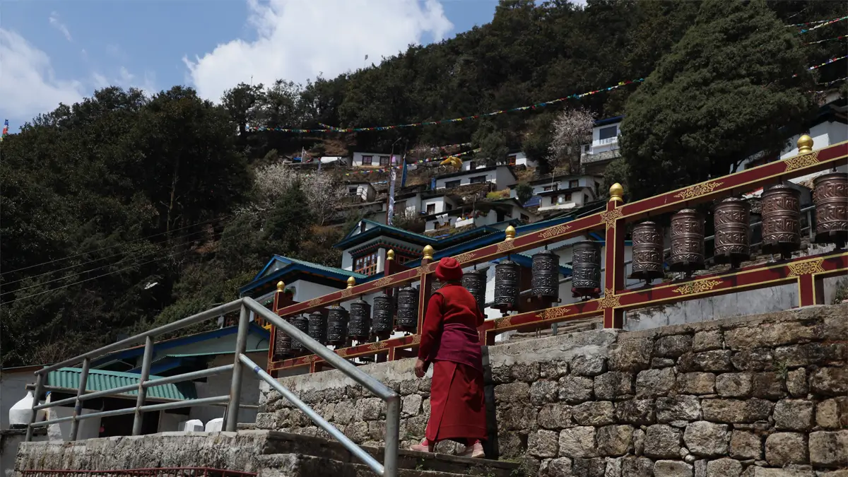 Monk walking up steps past a row of prayer wheels in Junbesi