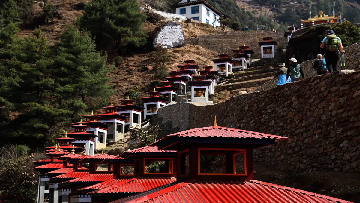 Row of red-roofed prayer wheel shrines climbing a hillside in Junbesi