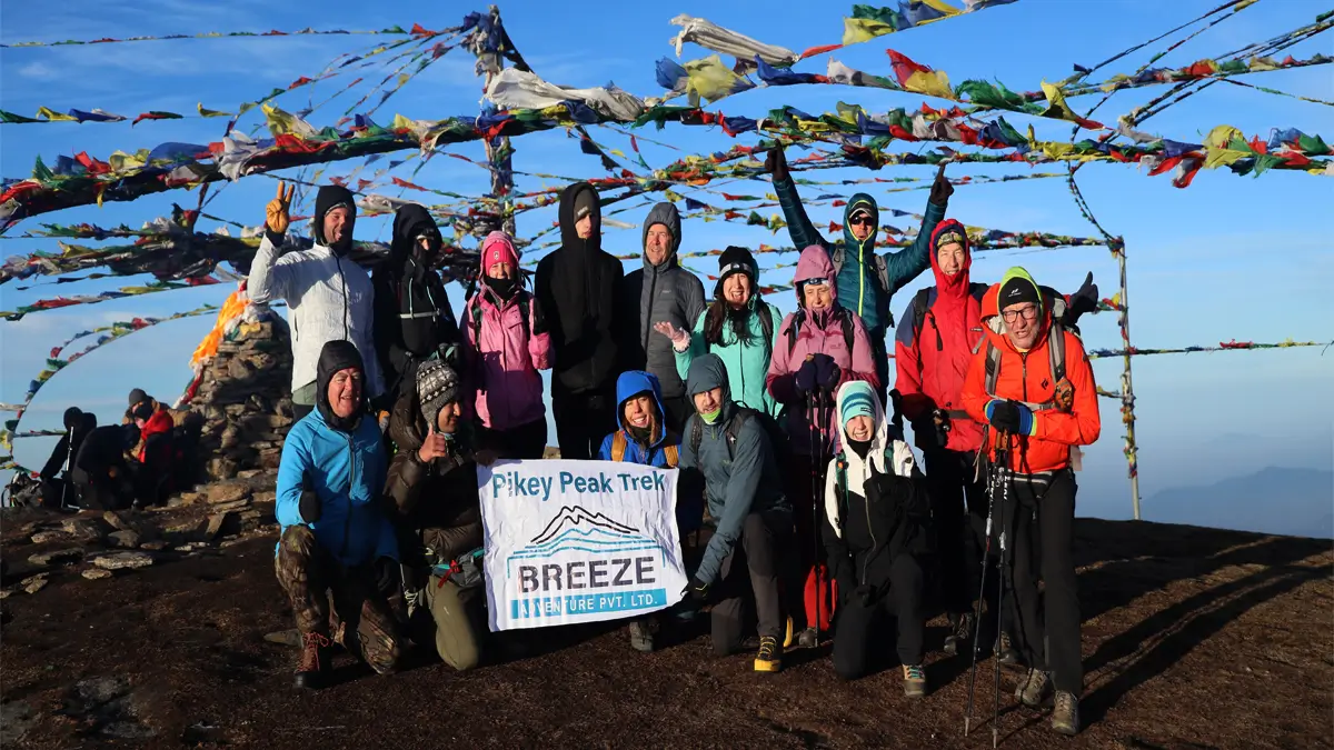 Trekking group at Pikey Peak summit with prayer flags and Breeze Adventure banner