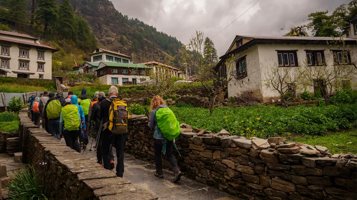 Trekkers walking a stone path through Junbesi village with rain-covered packs