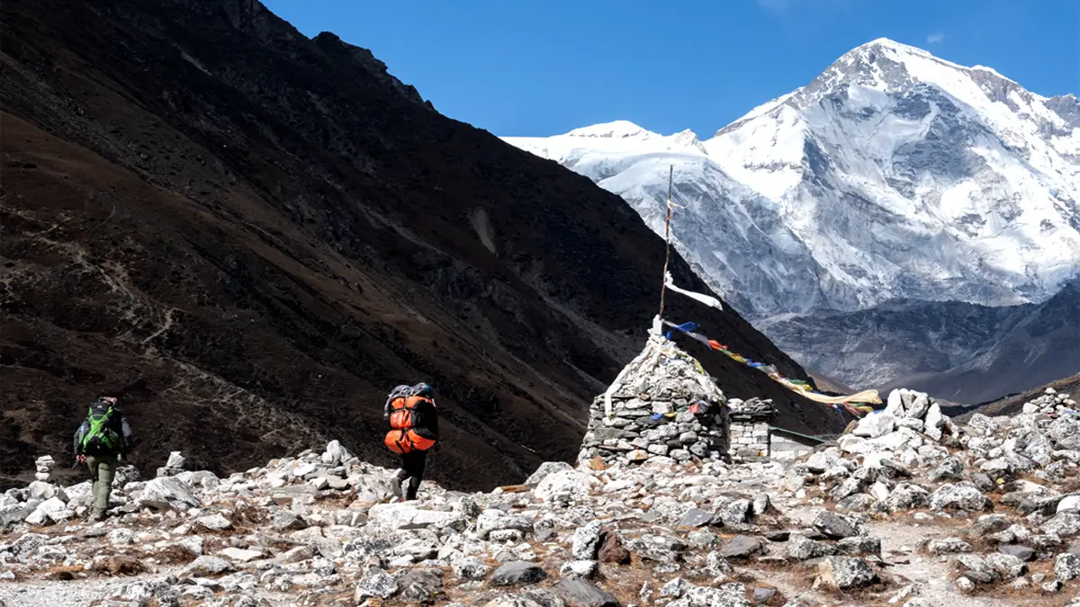 Two trekkers passing a stone chorten on a high Himalayan trail in the Everest region