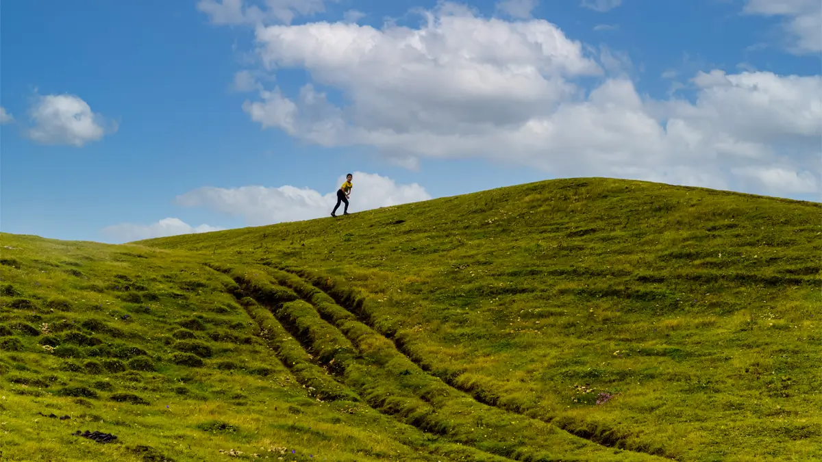 A lone trekker walking up a green grassy hill under a blue sky in spring