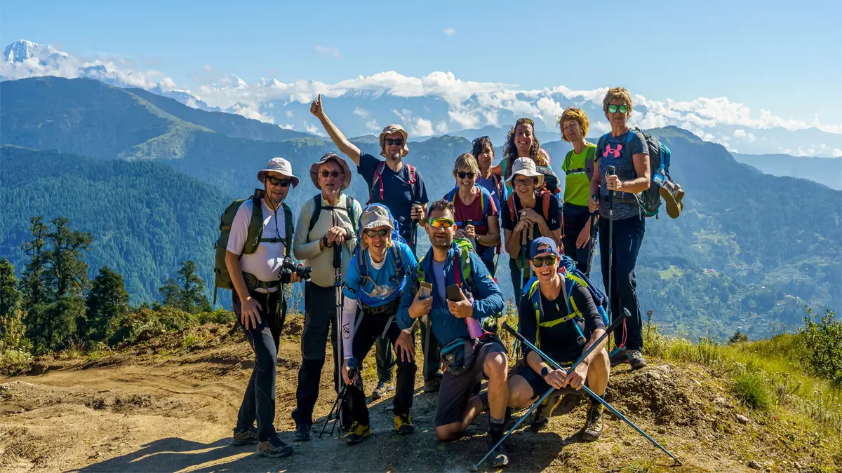 roup of trekkers posing on a ridge with forested hills and distant Himalayan peaks