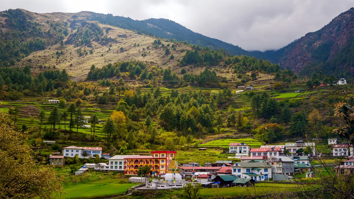 Junbesi village with terraced green fields, pine forest, and a stupa below cloudy mountains in Nepal