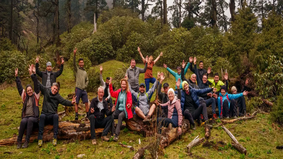 Group of trekkers posing happily in a mountain meadow surrounded by pine and rhododendron forest in Nepal