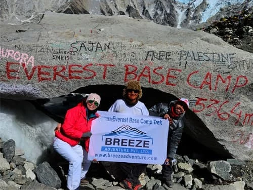 Group of trekkers at Everest Base Camp rock with Breeze Adventure banner, Khumbu Glacier in background